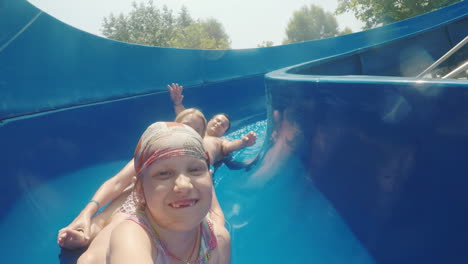 a happy family with a child is riding a water slide laughing waving their hands at the camera slow m