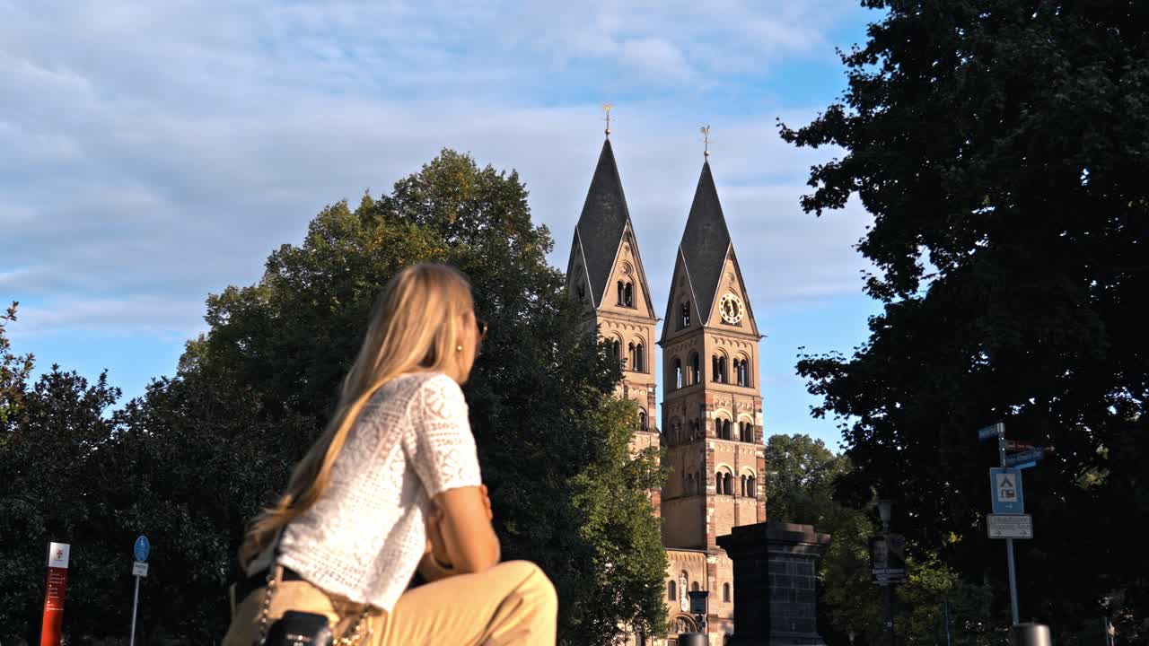 A low-angle, scenic shot of the historic Basilica of St. Castor in Koblenz, Germany, with its twin Romanesque towers and dark pyramidal roofs dominating the background