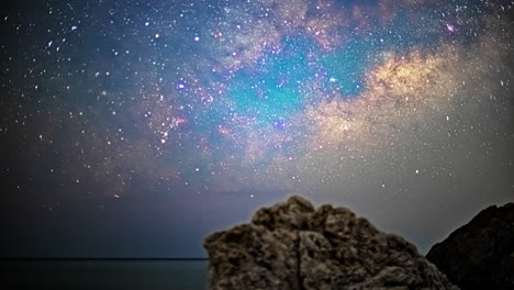 timelapse captures comets streaking across the night sky above rocky boulder, with ocean in the background