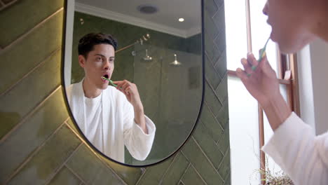 biracial man brushing teeth in morning, looking in bathroom mirror, slow motion