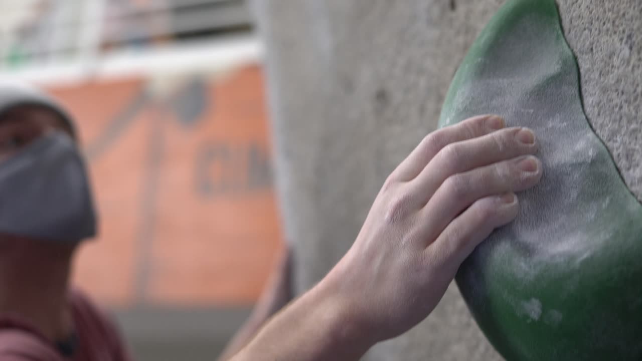 Rock climber climbing an indoor rock wall using athletic chalk for grip.