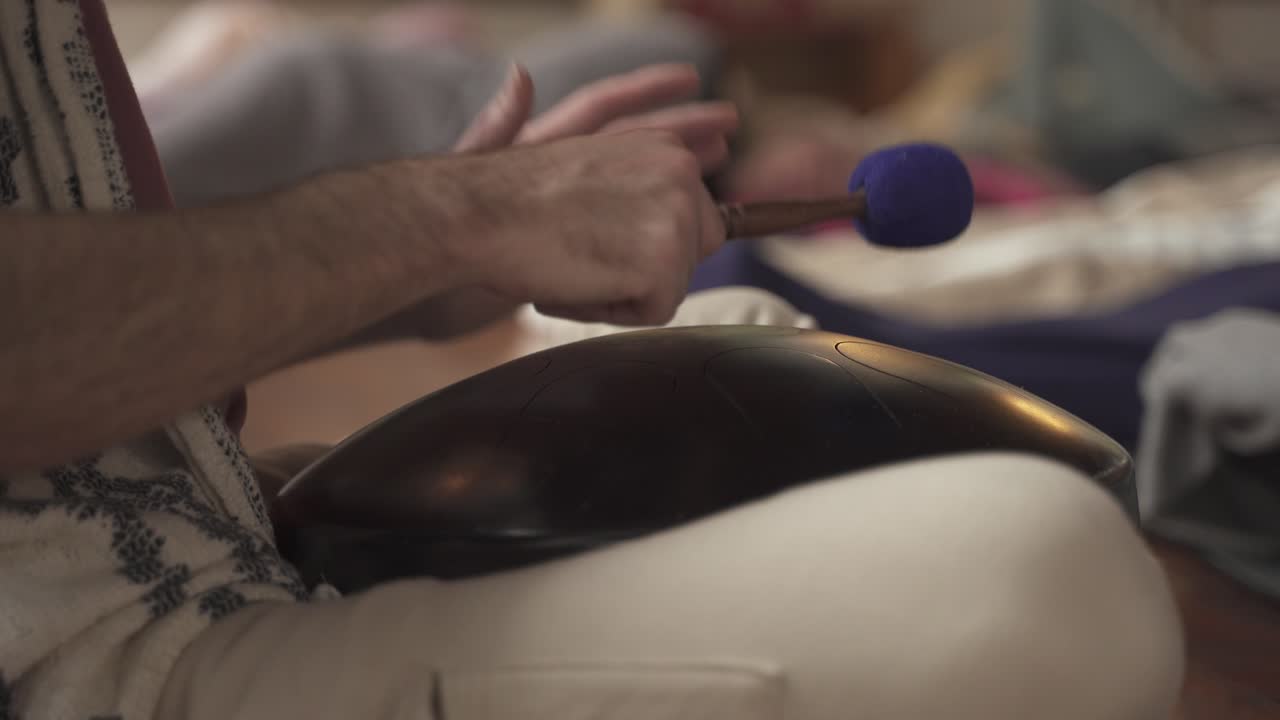 un hombre toca un tambor handpan en un ritual de curación de sonido