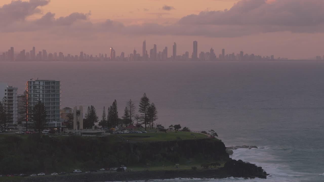 Horizonte da Gold Coast silhuetado contra um pôr do sol nebuloso, visto dos penhascos de Point Danger em Queensland, Austrália. Ampla tomada de drone.