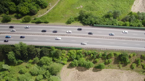 Luftaufnahmen-Von-Oben-Nach-Unten-Des-Verkehrs-Auf-Asphaltierter-Autobahn,-Umgeben-Von-Waldbäumen-Und-Feldern-Im-Sommer