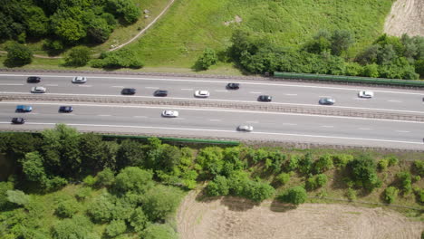 toma aérea de arriba hacia abajo del tráfico en la carretera asfaltada rodeada de árboles y campos forestales en verano