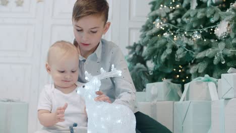 Closeup-two-lovely-siblings-sitting-with-glowing-deer-on-floor.