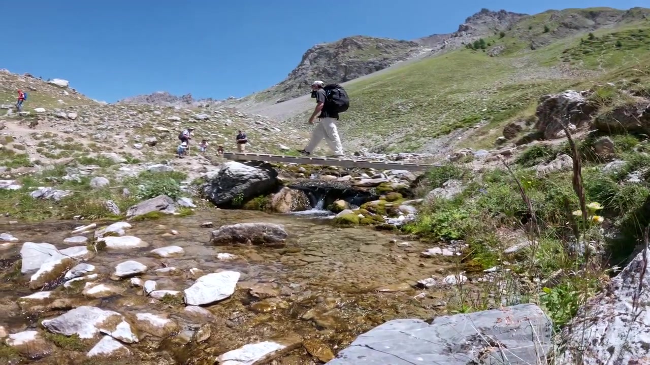 Zainisti camminano su uno stretto ponte di legno sopra un ruscello di montagna poco profondo in una giornata di sole