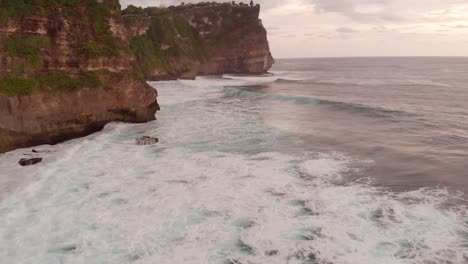 aerial cinematic shot of vibrant beautiful sunset over huge cliffs in uluwatu bali with deep blue crashing waves at the base of the ocean-4