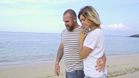 cheerful couple embracing and walking on ocean beach