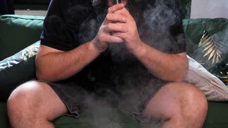 a man takes a drag from an e-cigarette and blows out a cloud of smoke