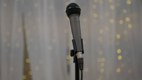 Wedding-Day-stock-clip-of-mic-microphone-on-stand-with-led-bokeh-lights-in-background-and-white-backdrop-ready-for-performer-singer-artist-or-toast-speeches,-slowly-panning-and-pushing-in