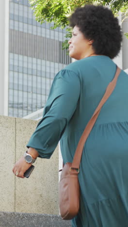 happy plus size biracial woman walking on stairs with smartphone in city