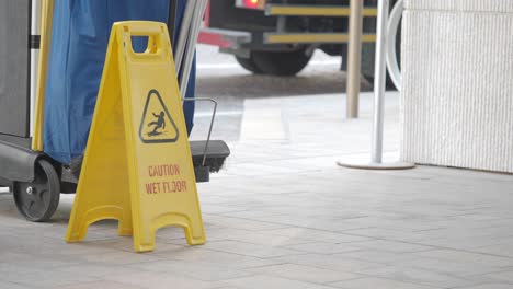 wet floor caution sign on a sidewalk with cleaning cart