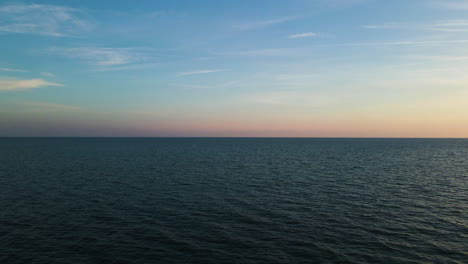 gentle soft glow of sunrise spreads across open ocean water texture, drone dolly