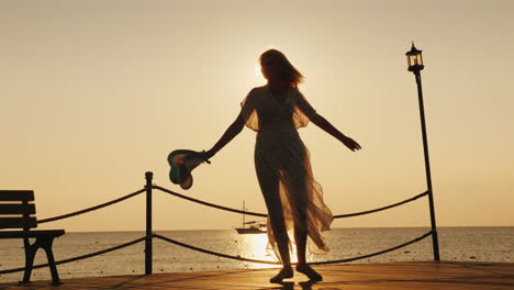 a woman meets the dawn at sea emotionally spinning with a hat in his hand on the pier dream of trave