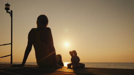 a woman sits on a pier next to a toy hare together they meet the sunrise over the sea romantic mood
