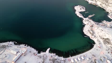 Aerial-view-of-a-snowy-coastal-town-at-twilight-with-clear-turquoise-waters