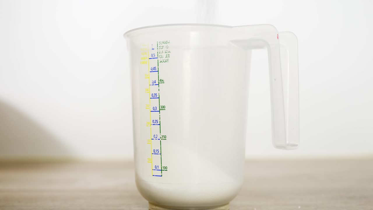 Side view shows sugar being poured into a measuring bowl, an early step in dessert preparation.