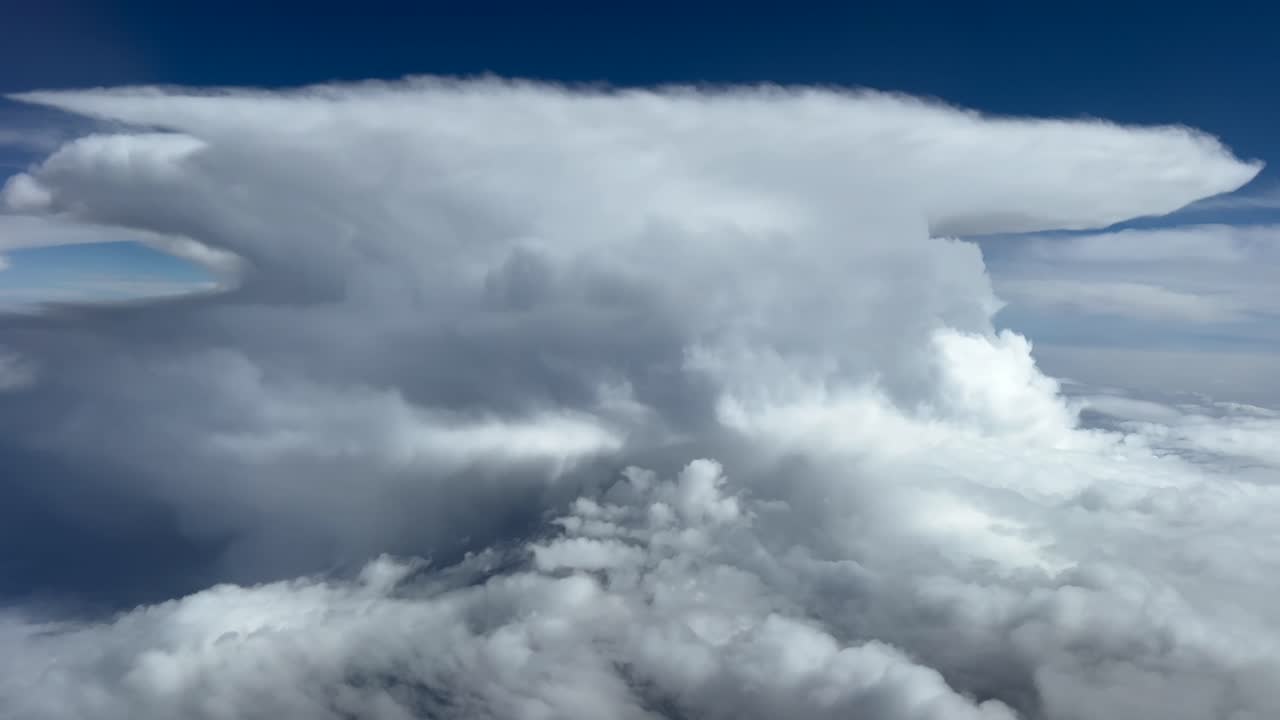 A massive storm cloud seen from above the sky. POV FPV aerial footage taken from an airplane cockpit flying through a stormy sky.