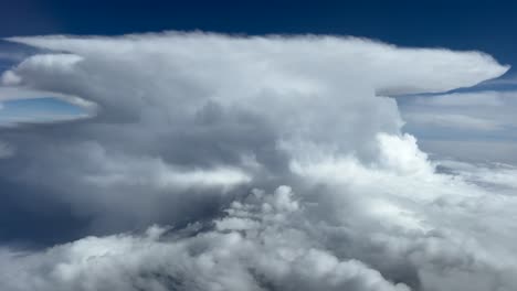 a massive storm cloud seen from above the sky. pov fpv aerial footage taken from an airplane cockpit flying through a stormy sky.