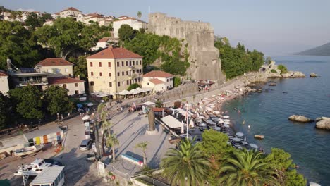 orbiting shot of herceg novi small beach by promenade with forte mare fortress in background, montenegro