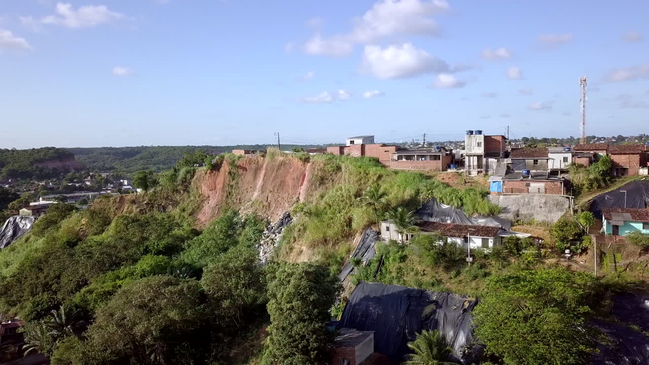 Drone flight over the Macaxeira area in Recife Pernambuco captures a daytime scene of a hillside community with simple houses vehicles and numerous tarps signifying poverty hazard and social disparity