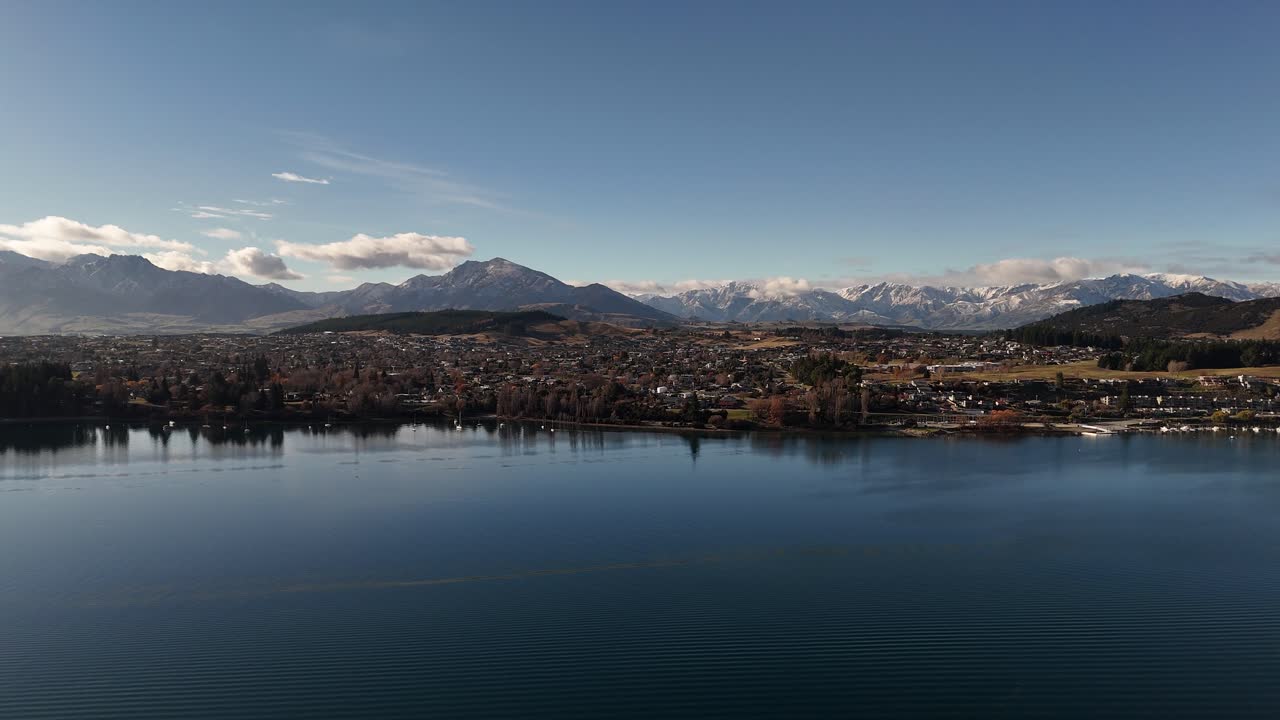Cinematic 4K 60fps drone shot flying backwards to reveal Lake Wanaka, the town, and the majestic Southern Alps. A perfect opening shot for travel videos or projects about New Zealand