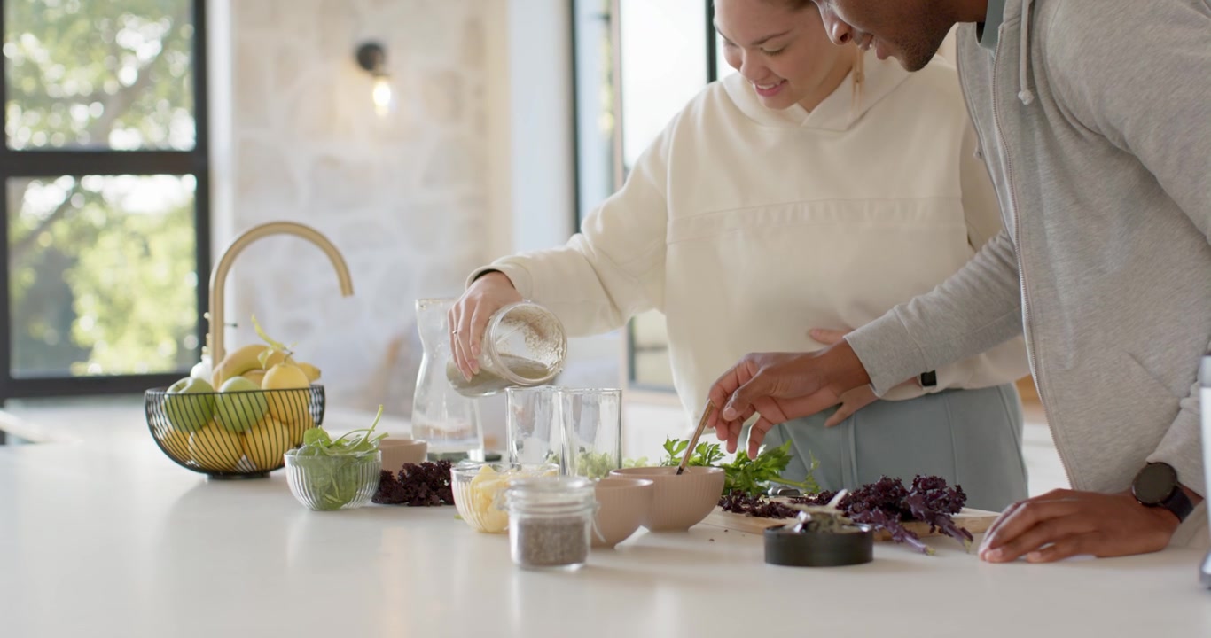 African American couple woman raising mason jar as man holding, pouring dressing on kitchen island
