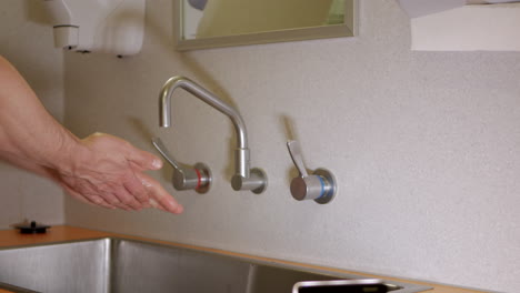 man uses elbow to turn on tap in hospital and wash hands