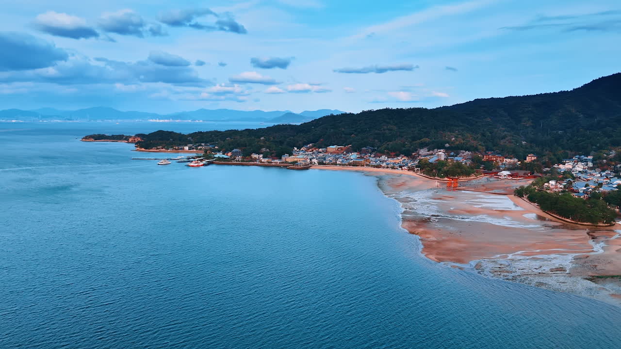 Amazing coast of the Inland Sea in Japan at the Miyajima island. Famous Itsukushima Shrine scenery from aerial view. Boat crosses the azure waterscape.