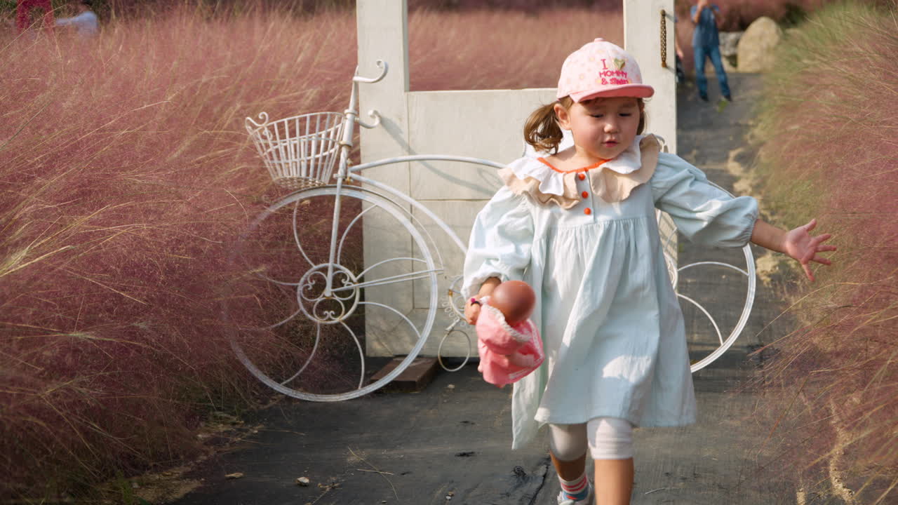 작은 소녀 유아가 분홍색 muhly 잔디 필드 또는 muhlenbergia capillaris에서 놀고 있습니다.