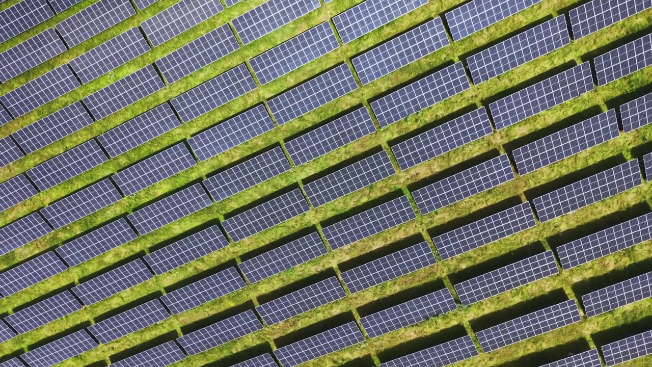 Terreno curvo che ospita schemi ripetitivi di pannelli solari con ombre. Prospettiva aerea che mostra dense installazioni fotovoltaiche con strade di servizio e ombre pomeridiane.