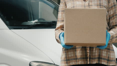 a delivery service worker holds a parcel standing near a van