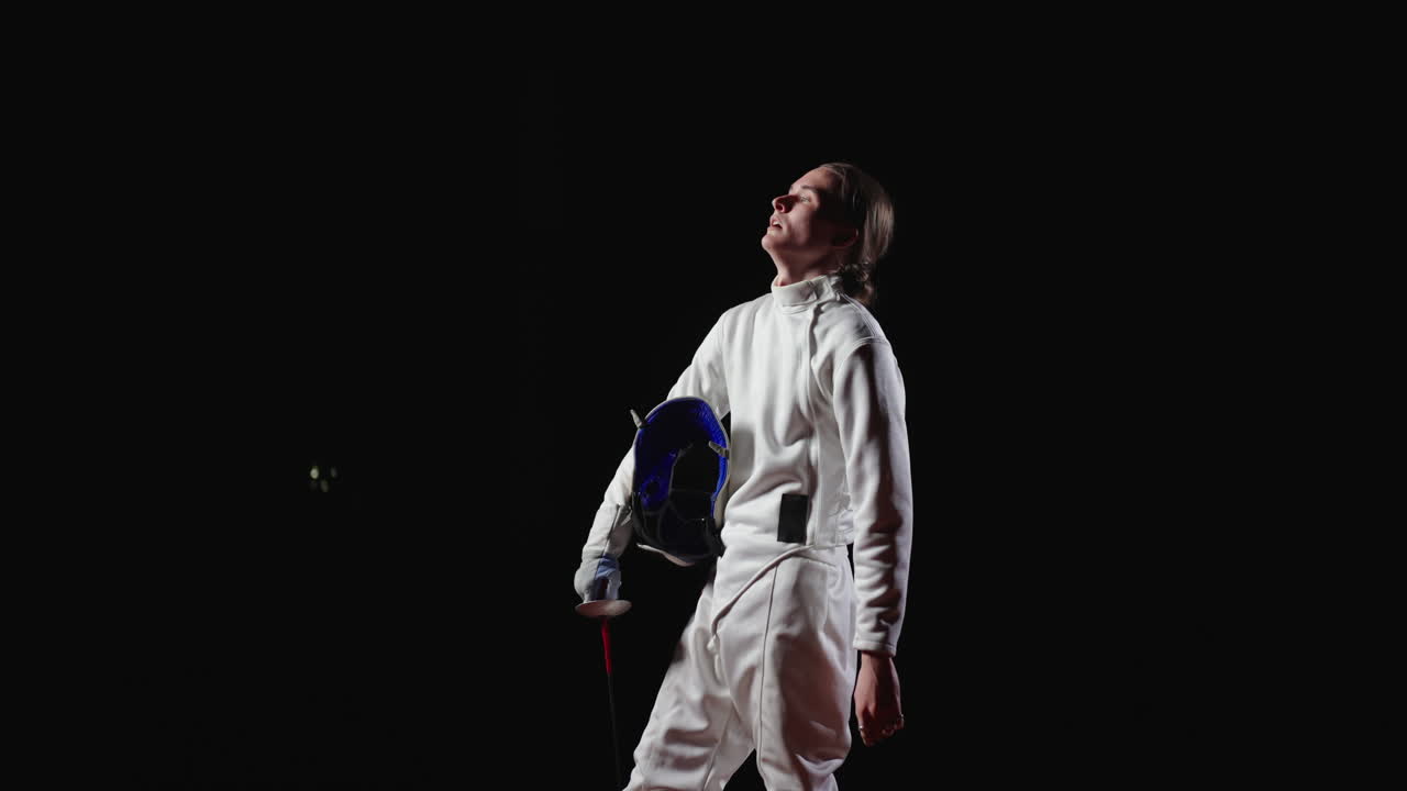 Young woman fencer in white uniform with foil and mask looking up