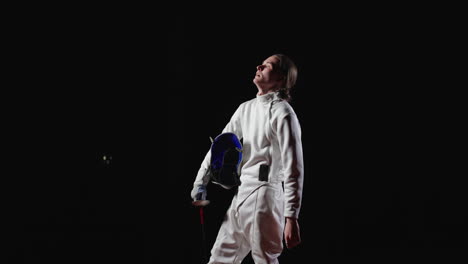 young woman fencer in white uniform with foil and mask looking up