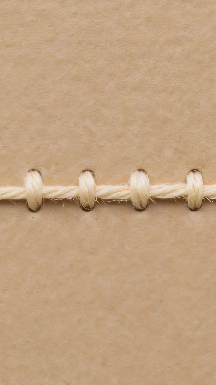 Vertical video: Camera panning over cream thread loops in holes on tan card at desk showing fray