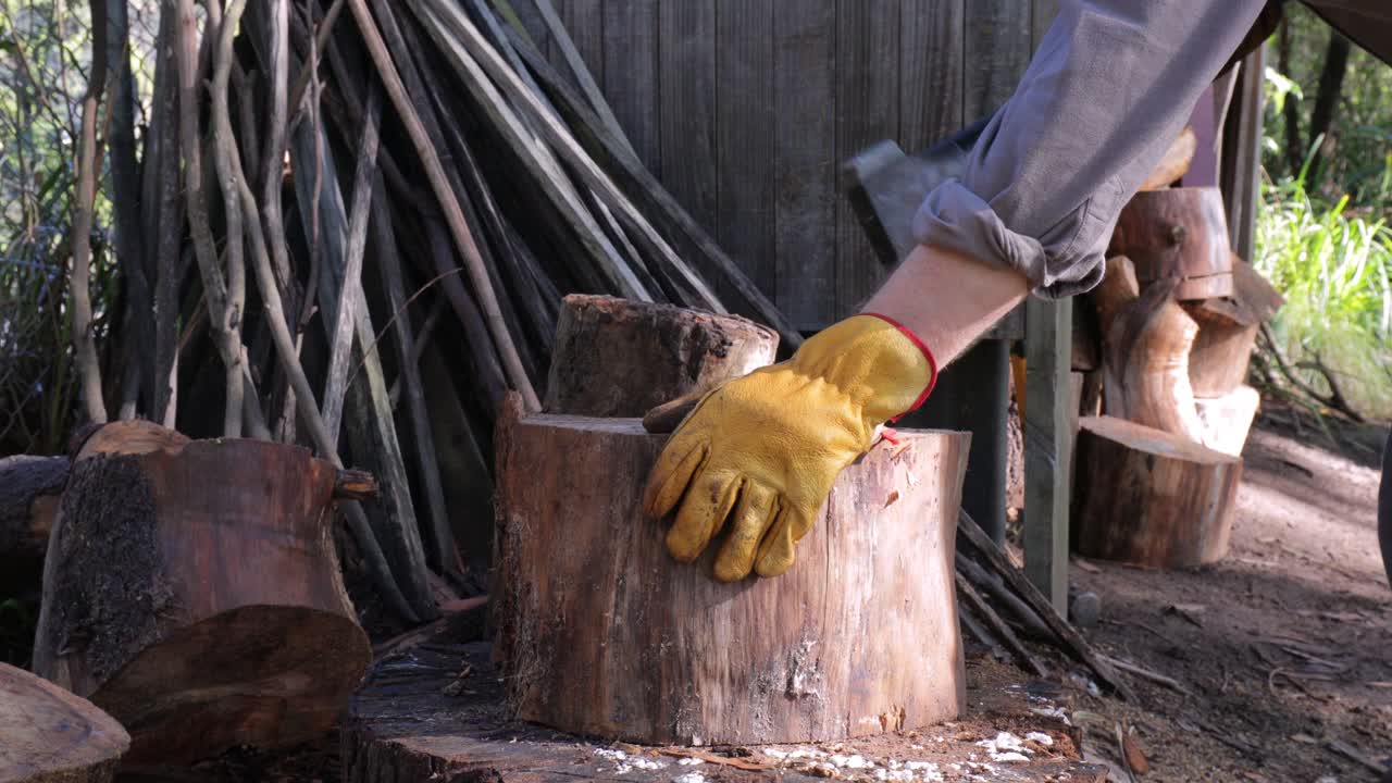 el hombre recoge el hacha y parte los troncos en la tienda de madera para obtener combustible de invierno - cierre del hacha, tronco, hombre en el trabajo, piernas, botas de trabajo y guantes de trabajo - 4k 59