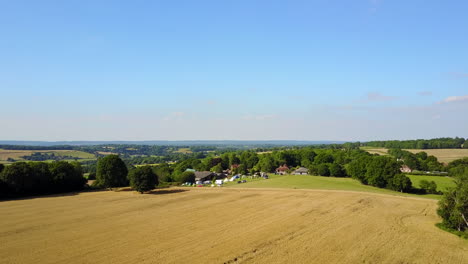 Kent-Countryside,-UK---Drone-flies-over-wheatfield-at-sunset-towards-small-campsite