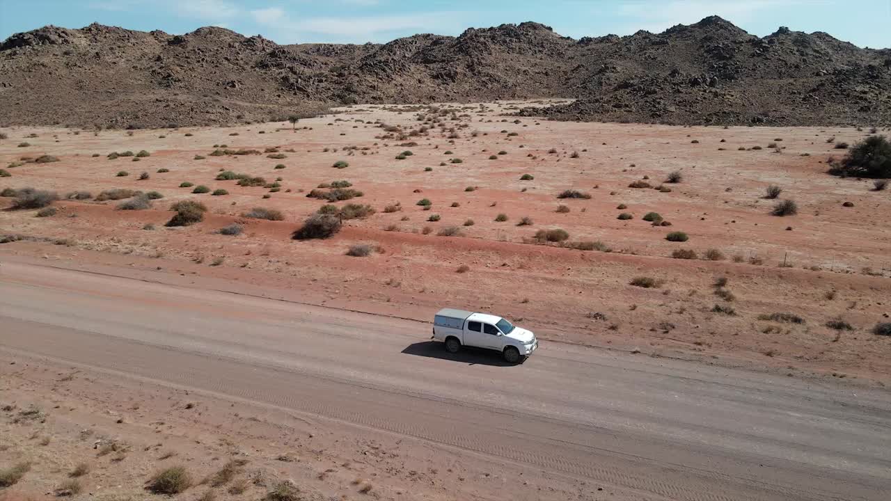 A sleek white Toyota Hilux glides through Namibia's Martian-like landscape, its rugged elegance conquering endless dusty roads