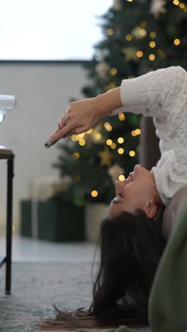 young woman using phone by christmas tree