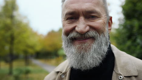 Close-up-portrait-of-bearded-man-looking-at-camera-outdoors.-Happy-senior-.
