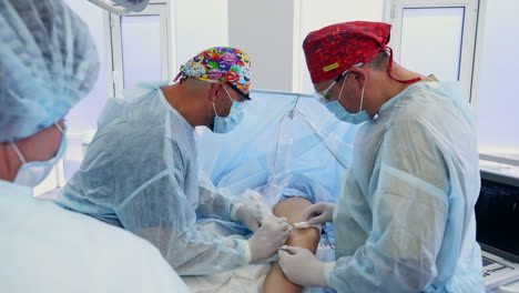 two surgeons in bright caps performing vascular operation. medics using metal instruments to operate the patient's leg.