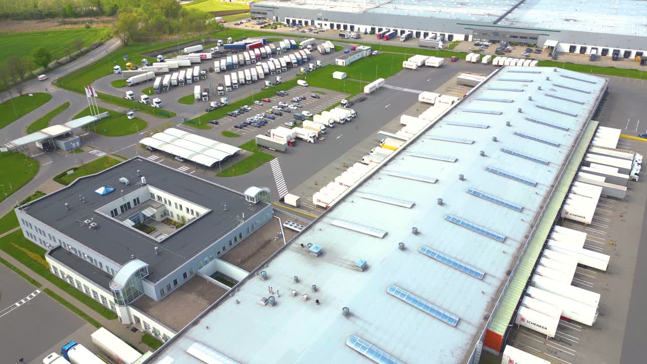 Droneoversigt over en gruppe store moderne industrilagre eller fabriksbygninger i et forstadsområde.