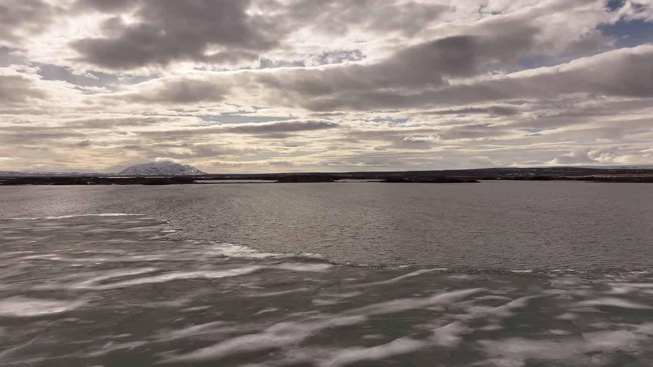 Waves and ice patterns form on the surface of a frozen Lake Mývatn under dramatic skies. Iceland