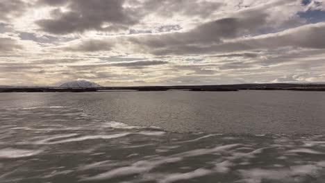 waves and ice patterns form on the surface of a frozen lake mývatn under dramatic skies. iceland