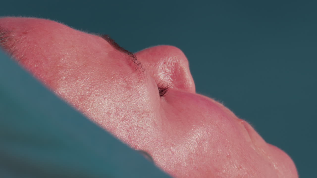 Cannes, France - October 10, 2025: Extreme close up of a man's face resting under the sun, skin glistening in the heat