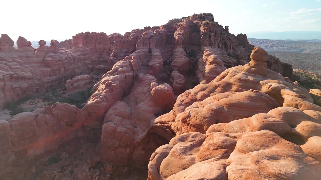 Splendido filmato stock del Parco Nazionale di Arches, USA, durante un pomeriggio luminoso. La luce solare brillante illumina le maestose strutture di arenaria rossa e il paesaggio desertico sotto un cielo azzurro limpido.