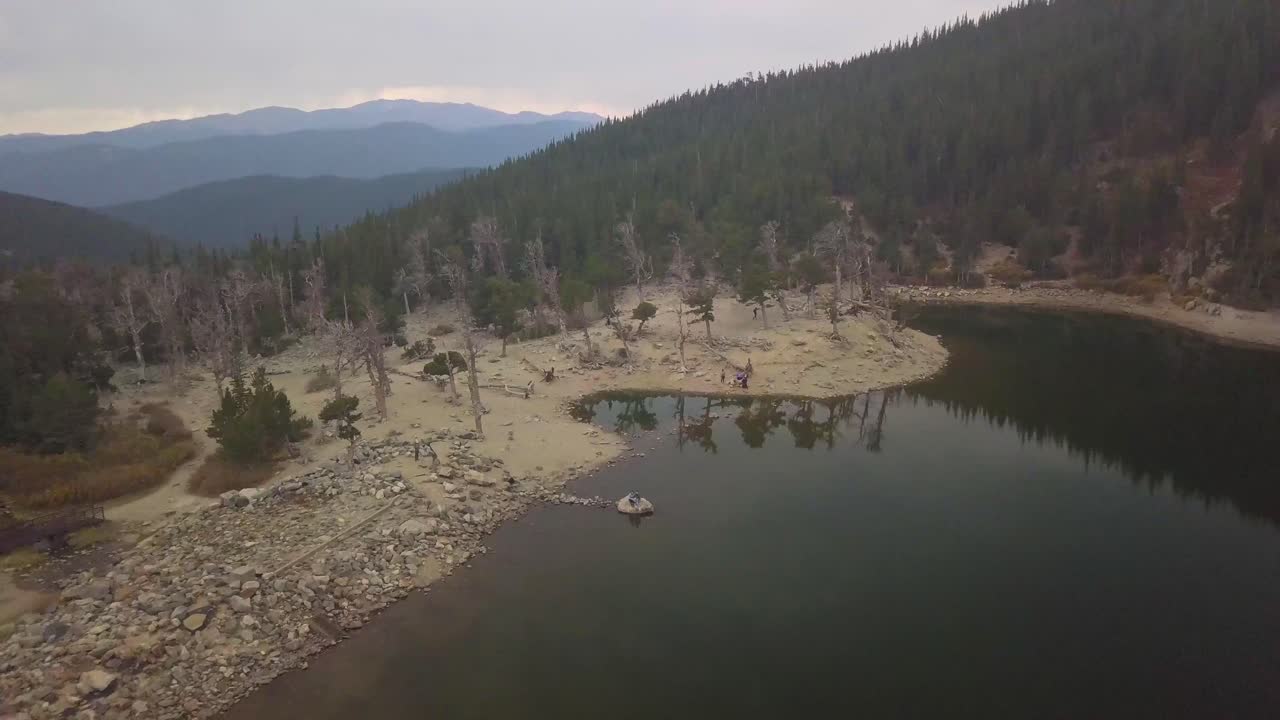 un carrello pullback di un paio di persone sedute su una roccia nel mezzo di un lago alpino