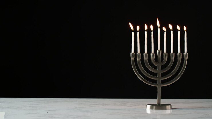 Lockdown shot of candles burning in a menorah against a black background, space on the left side of frame