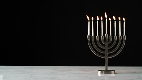 lockdown shot of candles burning in a menorah against a black background, space on the left side of frame